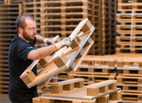 Logistieke medewerker stapelt houten pallets in een magazijn